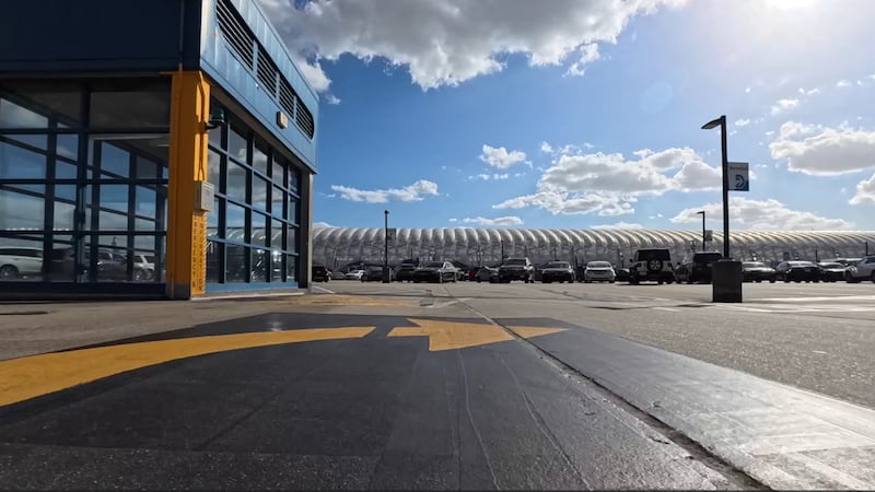 A parking lot at an airport. A row of cars is seen along with an arrow pointing the direction...